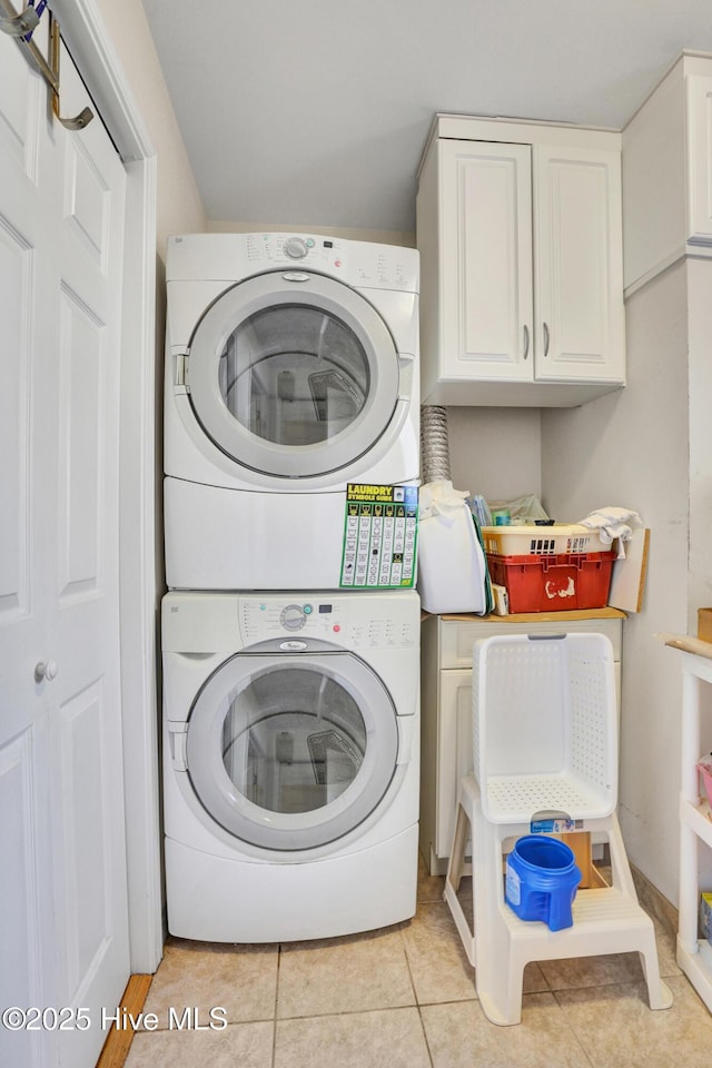 clothes washing area featuring stacked washer / drying machine, light tile patterned floors, and cabinets