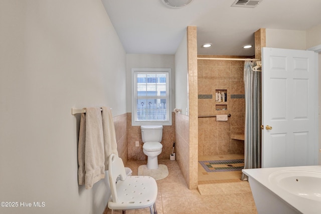 full bathroom featuring tile patterned flooring, a shower stall, a wainscoted wall, toilet, and tile walls