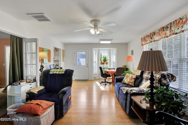 living room with a ceiling fan, visible vents, and light wood-type flooring