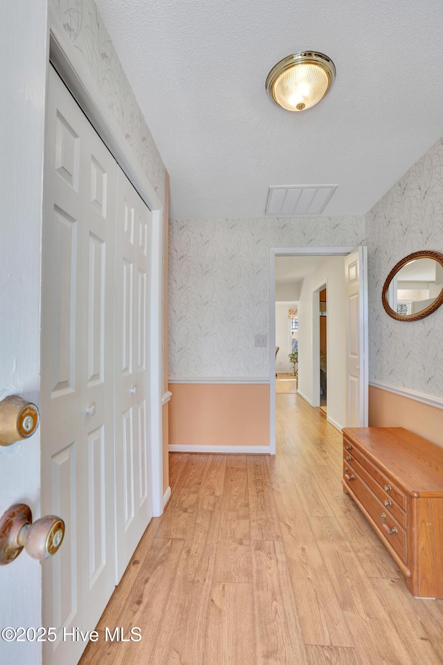 hall with a textured ceiling and light hardwood / wood-style floors