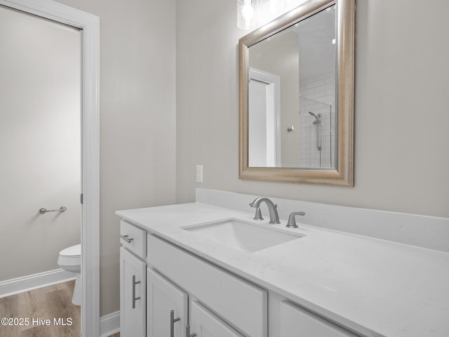 bathroom featuring toilet, vanity, wood finished floors, and baseboards