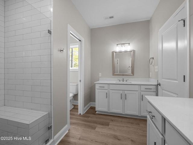 full bath with visible vents, baseboards, toilet, vanity, and wood finished floors
