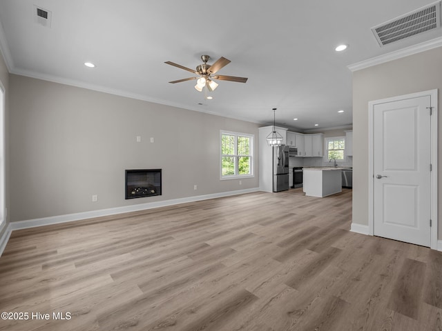 unfurnished living room featuring visible vents, a sink, ornamental molding, ceiling fan, and light wood-style flooring