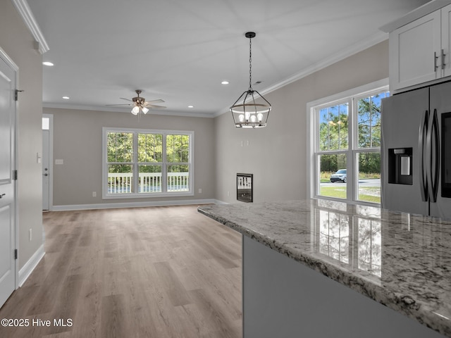 kitchen with crown molding, ceiling fan with notable chandelier, stainless steel fridge with ice dispenser, light wood-style floors, and light stone countertops