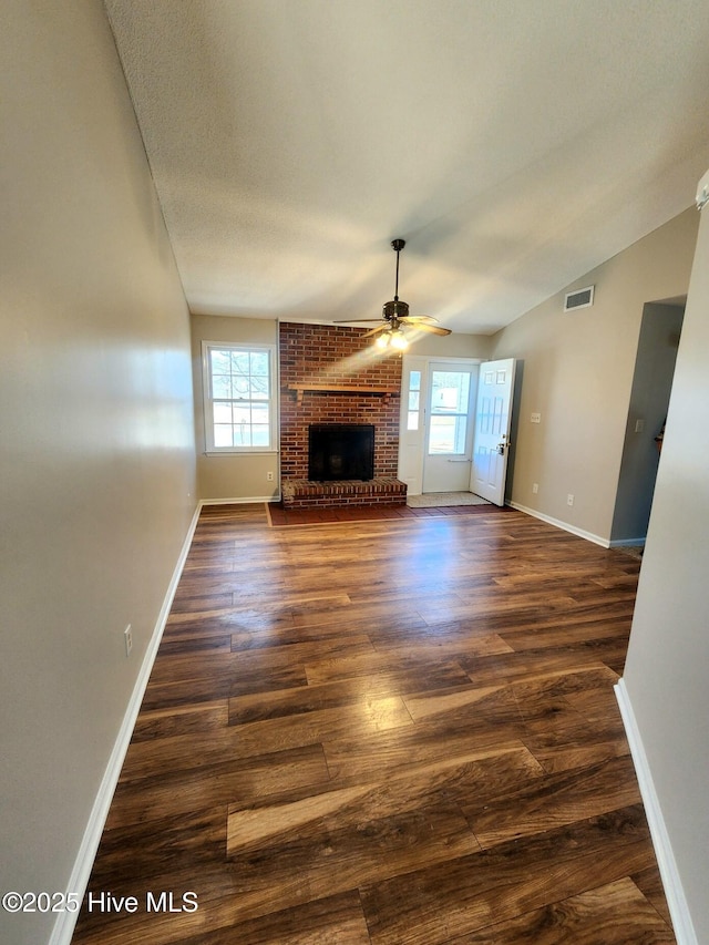 unfurnished living room with a brick fireplace, dark wood-type flooring, a healthy amount of sunlight, and vaulted ceiling