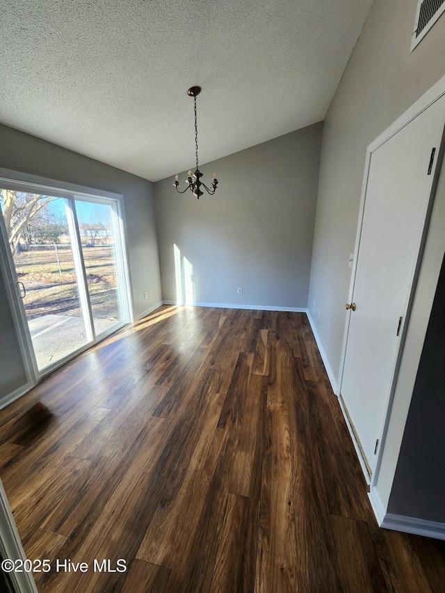 unfurnished dining area featuring dark hardwood / wood-style floors, a textured ceiling, and an inviting chandelier