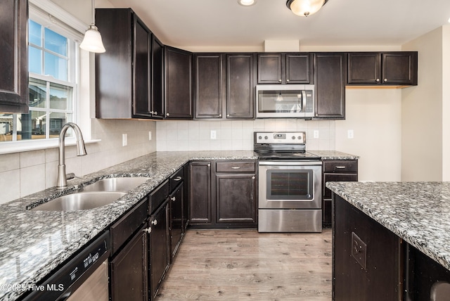 kitchen with dark stone counters, hanging light fixtures, sink, light wood-type flooring, and appliances with stainless steel finishes