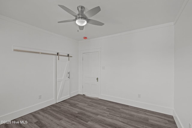 spare room featuring hardwood / wood-style floors, ceiling fan, a barn door, and ornamental molding