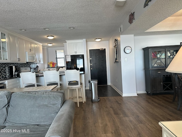 kitchen with backsplash, black refrigerator, range with electric cooktop, dark hardwood / wood-style flooring, and white cabinetry