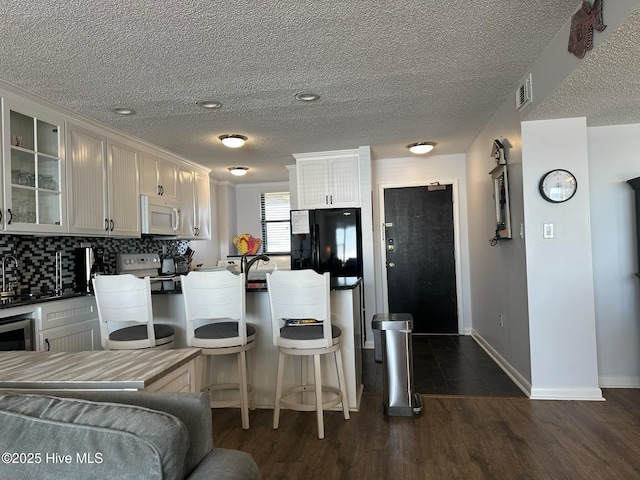 kitchen with dark wood-type flooring, white cabinets, black fridge, range with electric stovetop, and tasteful backsplash