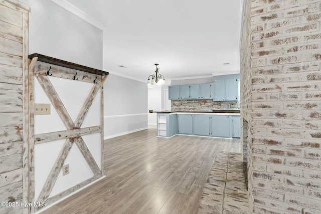 kitchen featuring hardwood / wood-style floors, hanging light fixtures, blue cabinetry, ornamental molding, and tasteful backsplash