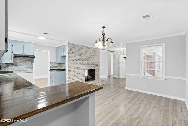 kitchen with butcher block counters, a notable chandelier, a brick fireplace, crown molding, and backsplash