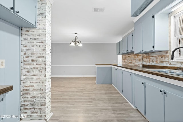 kitchen with sink, an inviting chandelier, light hardwood / wood-style flooring, hanging light fixtures, and crown molding