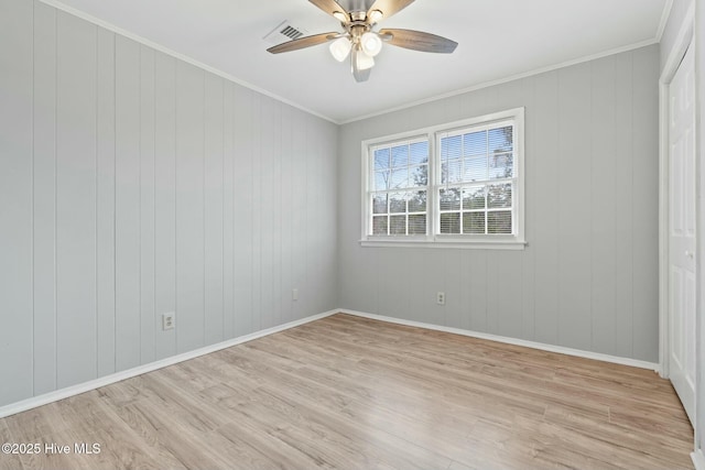 spare room featuring ceiling fan, light wood-type flooring, ornamental molding, and wooden walls