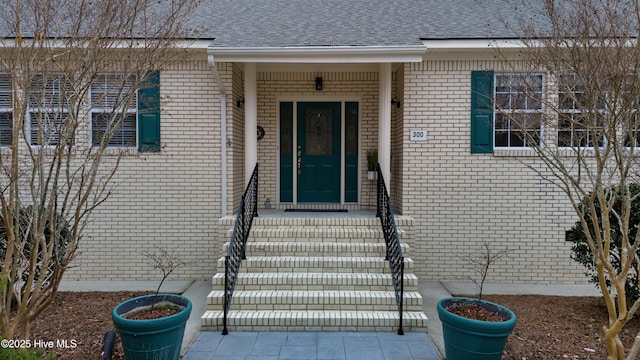 view of exterior entry with a shingled roof and brick siding