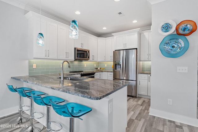 kitchen with a kitchen breakfast bar, stainless steel appliances, kitchen peninsula, white cabinetry, and backsplash