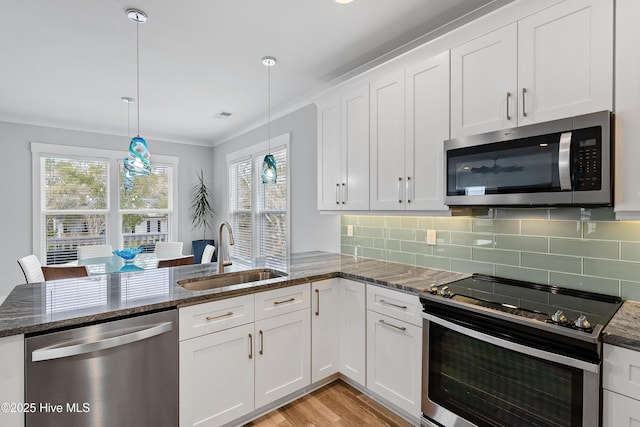 kitchen with kitchen peninsula, hanging light fixtures, white cabinets, appliances with stainless steel finishes, and sink