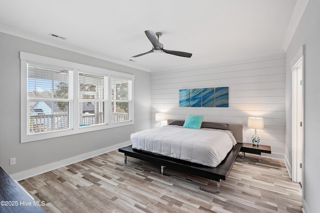 bedroom with ceiling fan, ornamental molding, light hardwood / wood-style floors, and wooden walls