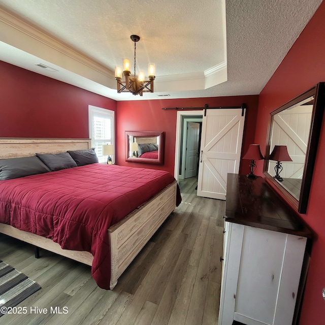 bedroom with crown molding, hardwood / wood-style flooring, a textured ceiling, a raised ceiling, and a barn door