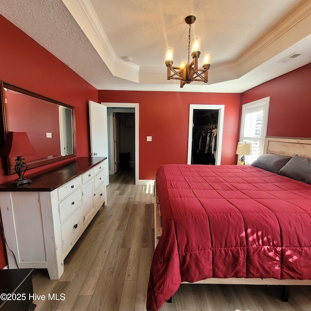 bedroom featuring crown molding, hardwood / wood-style flooring, a tray ceiling, a textured ceiling, and a spacious closet