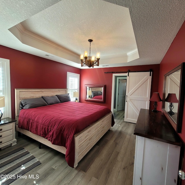 bedroom with a barn door, dark hardwood / wood-style floors, a tray ceiling, and a textured ceiling