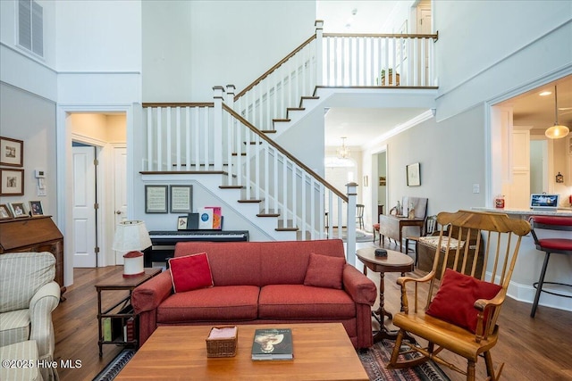 living room featuring stairway, visible vents, a towering ceiling, and wood finished floors