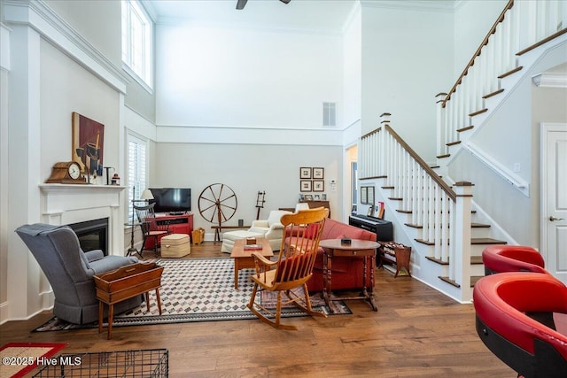 living room featuring a glass covered fireplace, ornamental molding, visible vents, and wood finished floors