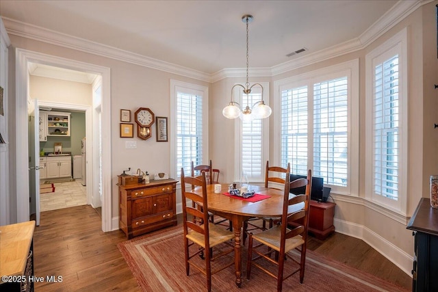 dining room featuring visible vents, wood finished floors, an inviting chandelier, crown molding, and baseboards