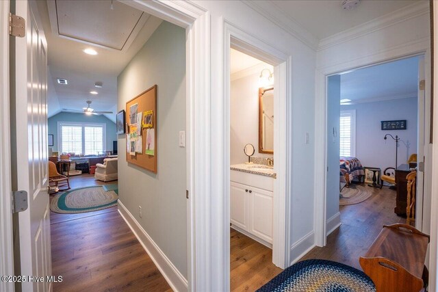 hallway with wood finished floors, baseboards, attic access, a sink, and crown molding