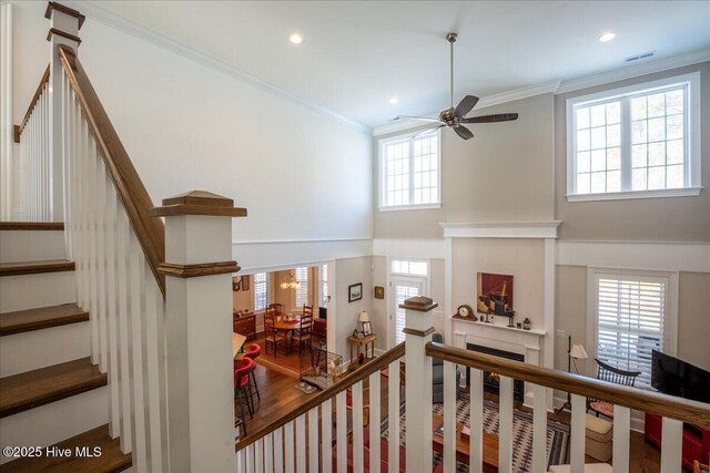 stairs with visible vents, wood finished floors, a fireplace, crown molding, and a towering ceiling