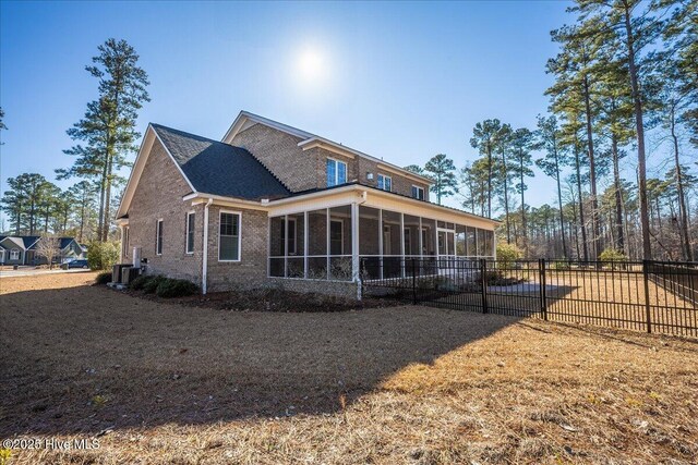 rear view of house with fence, brick siding, and a sunroom