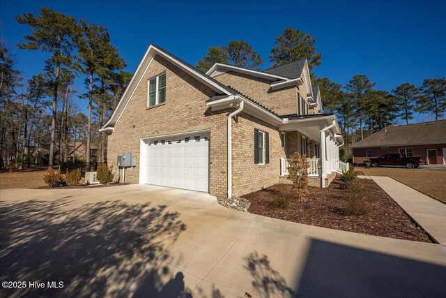 view of home's exterior with a porch, concrete driveway, an attached garage, and brick siding