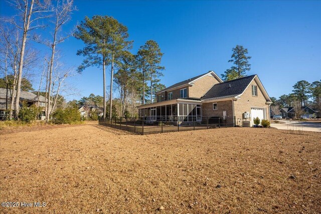 rear view of house featuring concrete driveway, fence, a garage, and a sunroom