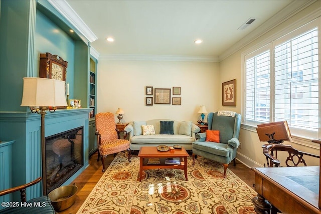 living room featuring a glass covered fireplace, visible vents, wood finished floors, and crown molding