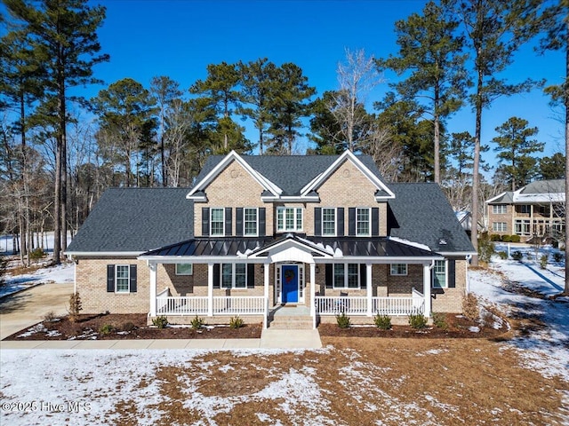 traditional-style house featuring a standing seam roof, a porch, roof with shingles, metal roof, and brick siding