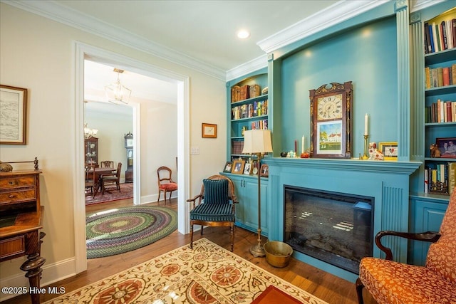 living area with built in shelves, wood finished floors, an inviting chandelier, ornamental molding, and a glass covered fireplace