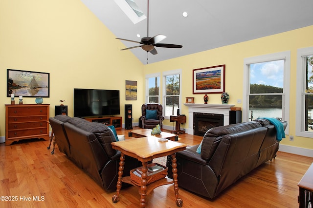 living room featuring ceiling fan, light hardwood / wood-style floors, high vaulted ceiling, and a skylight