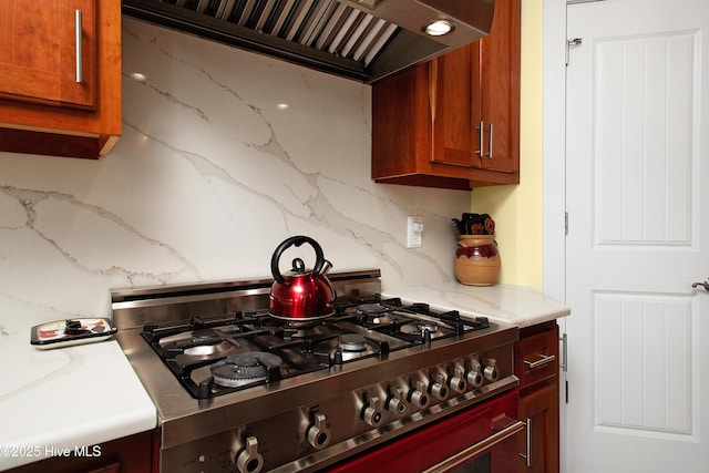 kitchen featuring wall chimney exhaust hood, backsplash, range, and light stone counters