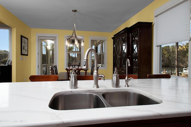 room details featuring sink, hanging light fixtures, an inviting chandelier, and light stone countertops