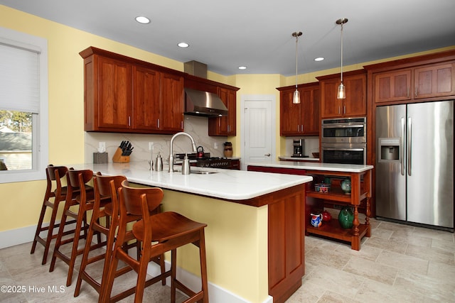 kitchen with appliances with stainless steel finishes, wall chimney exhaust hood, sink, hanging light fixtures, and kitchen peninsula