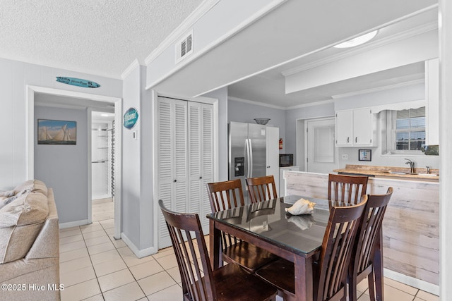 tiled dining room with sink, a textured ceiling, and ornamental molding