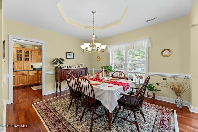 dining room with a tray ceiling, dark hardwood / wood-style flooring, and a notable chandelier