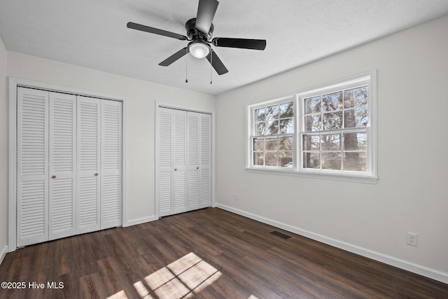 unfurnished bedroom with two closets, ceiling fan, and dark wood-type flooring