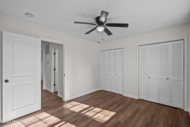 unfurnished bedroom featuring multiple closets, ceiling fan, and dark wood-type flooring