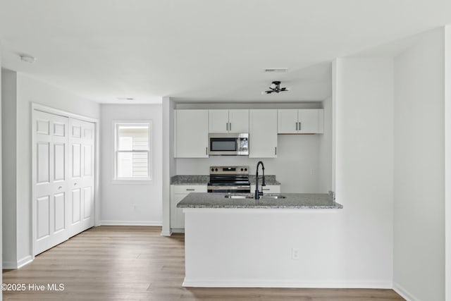 kitchen featuring light stone countertops, light wood-type flooring, stainless steel appliances, sink, and white cabinetry