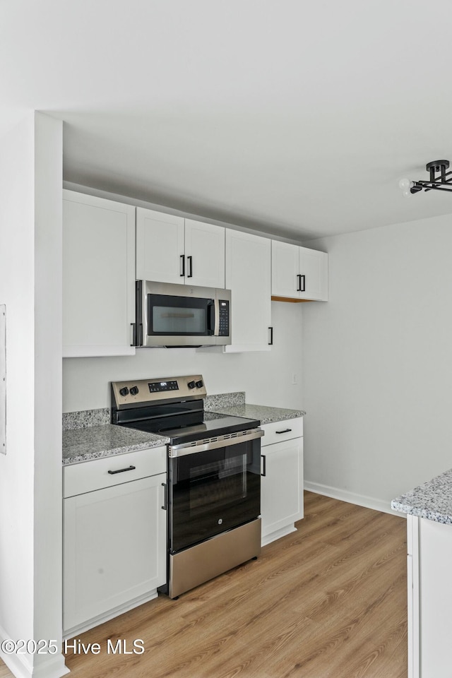 kitchen with white cabinets, light stone counters, stainless steel appliances, and light hardwood / wood-style flooring