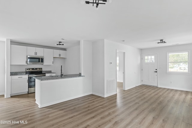 kitchen with white cabinets, sink, light hardwood / wood-style flooring, dark stone countertops, and stainless steel appliances