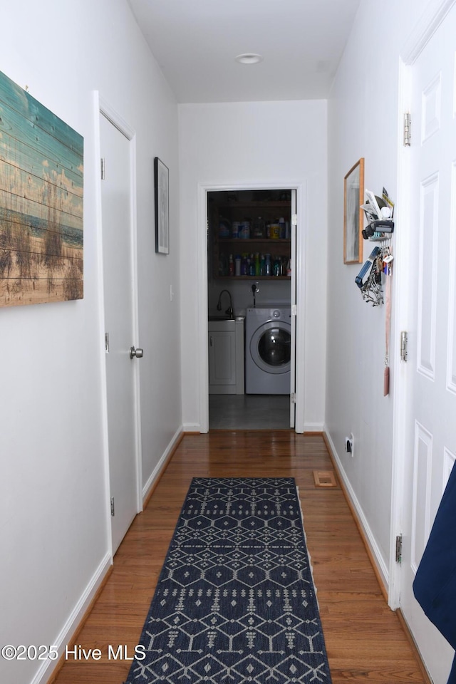 corridor with washer / clothes dryer, hardwood / wood-style flooring, and sink