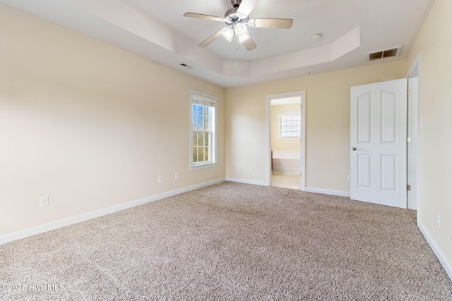 unfurnished bedroom with ceiling fan, ensuite bath, a tray ceiling, and carpet