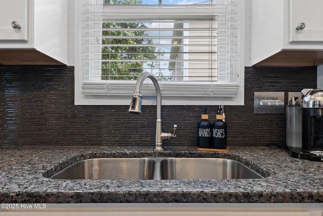 room details with white cabinets, tasteful backsplash, dark stone countertops, and sink